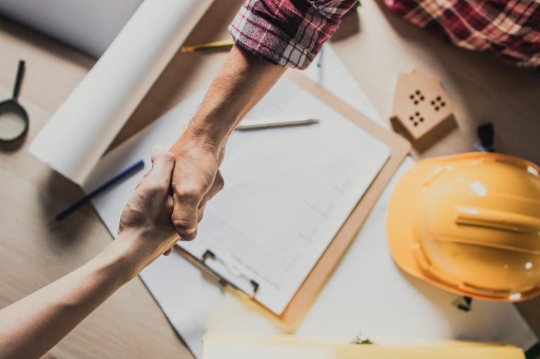 Two men in a construction site shake hands after finalizing a deal.