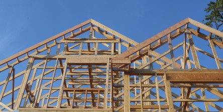 Wooden frame of a house under construction with clear blue skies, highlighting architectural framework and building development.